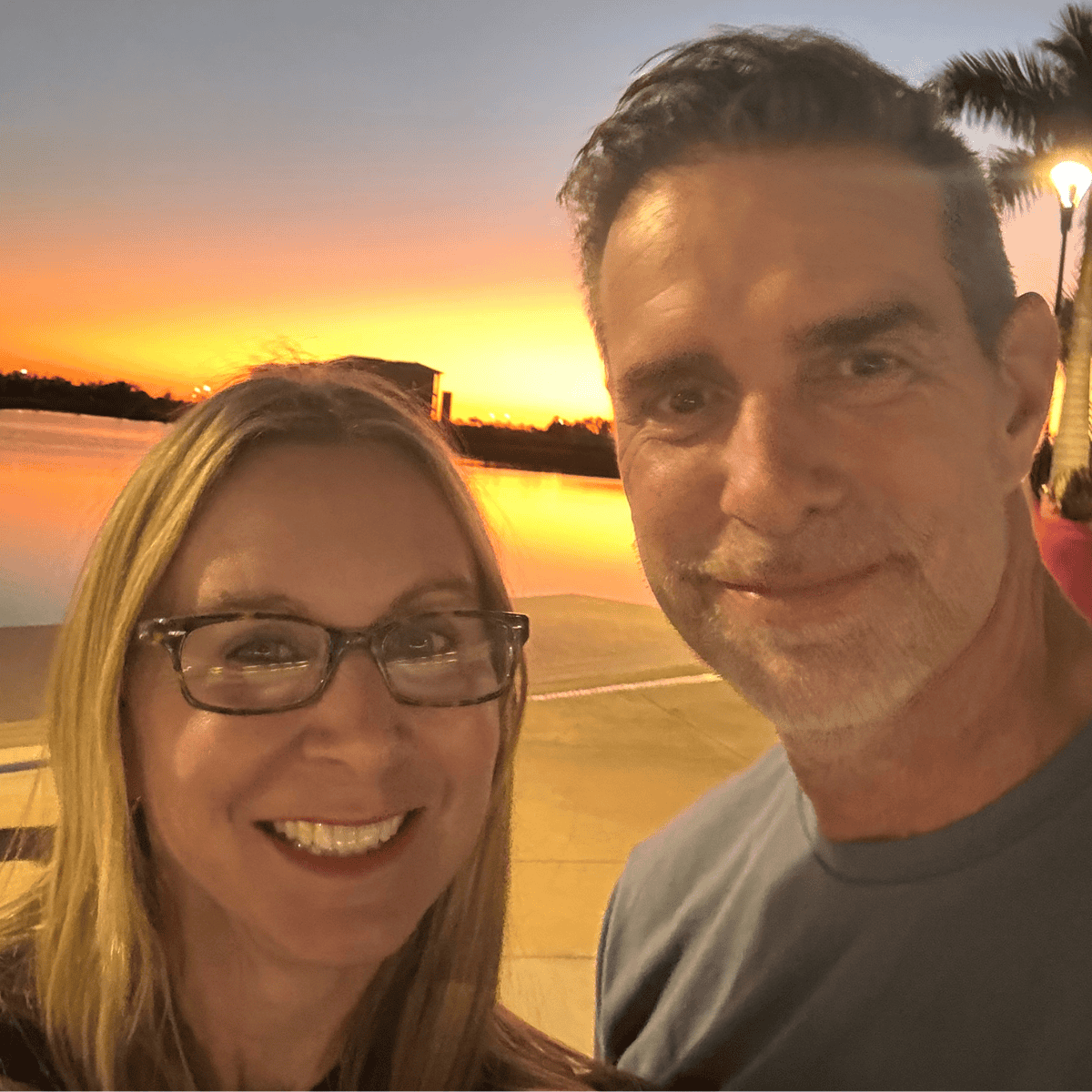Untitled design (21) Smiling couple taking a sunset selfie by a calm waterfront.
